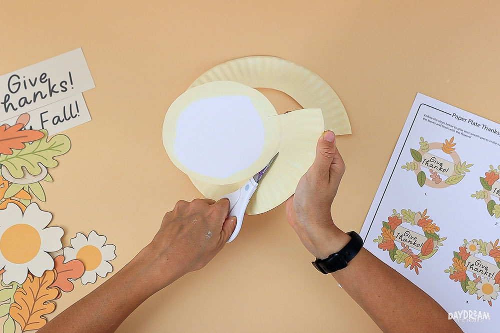 Cutting the center out of a paper plate to make the base for a kids’ Fall & Thanksgiving Paper Plate Wreath Craft