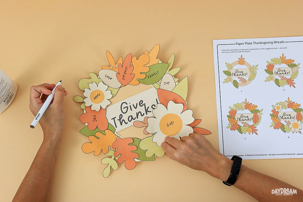 Thanksgiving paper plate wreath craft in progress with written why to give thanks for, autumn leaves, and free printable template for kids.