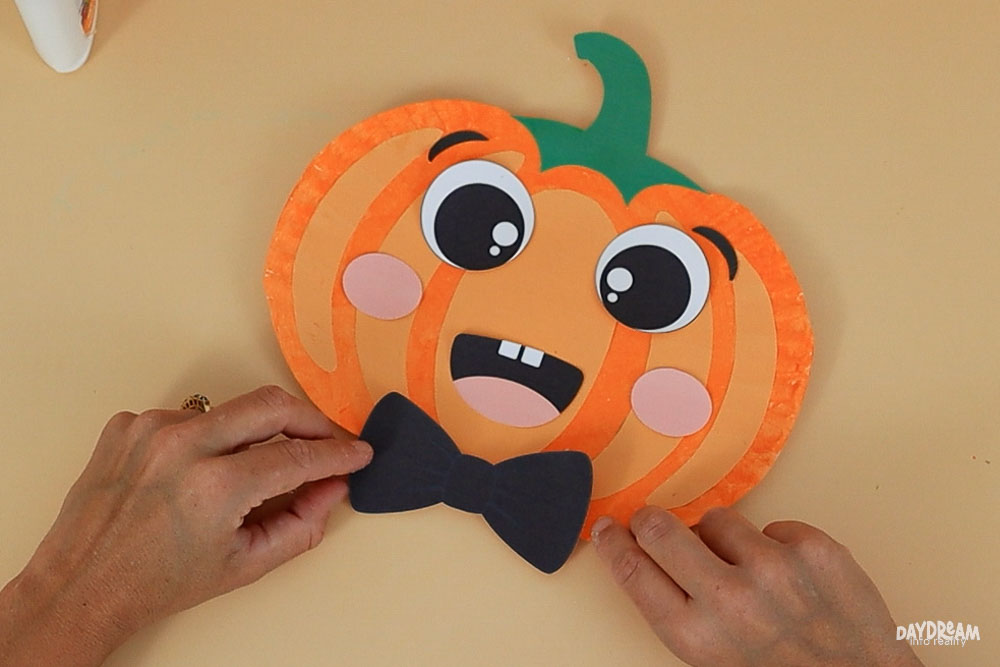 placing bow tie in paper plate pumpkin