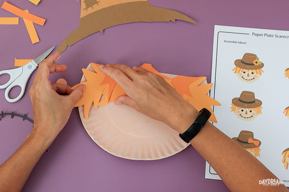 gluing jagged straw hair to paper plate scarecrow