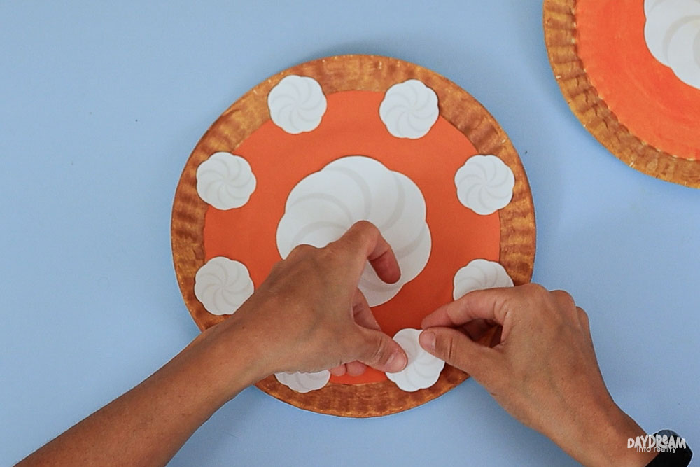 adding whipped cream dollops to the paper plate pumpkin pie